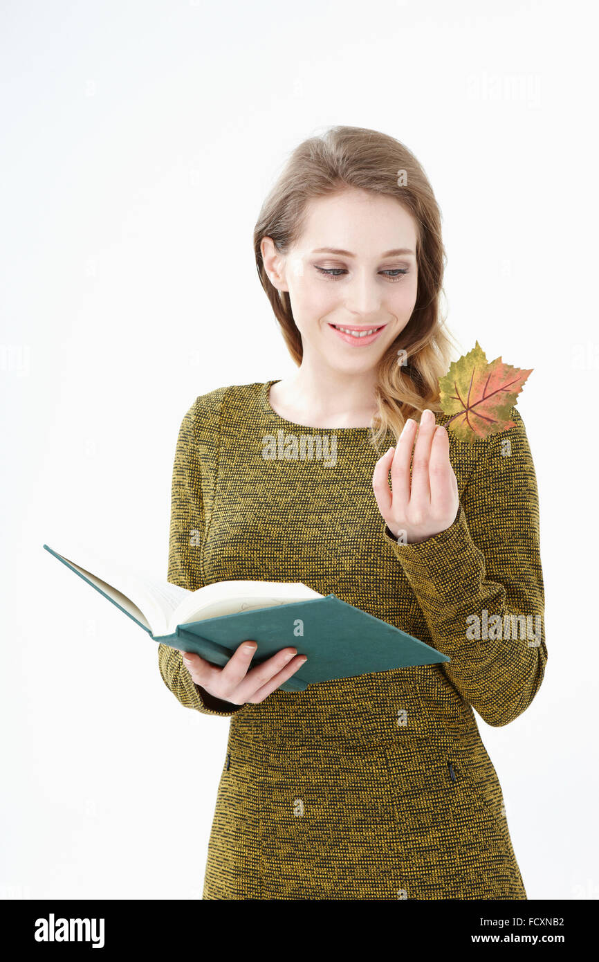 Portriat della giovane donna sorridente tiene un libro aperto e una foglia caduta guardando verso il basso Foto Stock