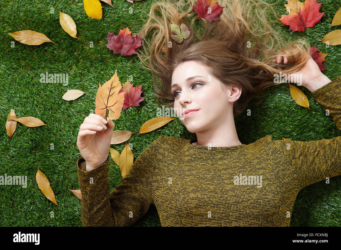 Ritratto di giovane donna con capelli lunghi sdraiati sull'erba con foglie cadute, Foto Stock