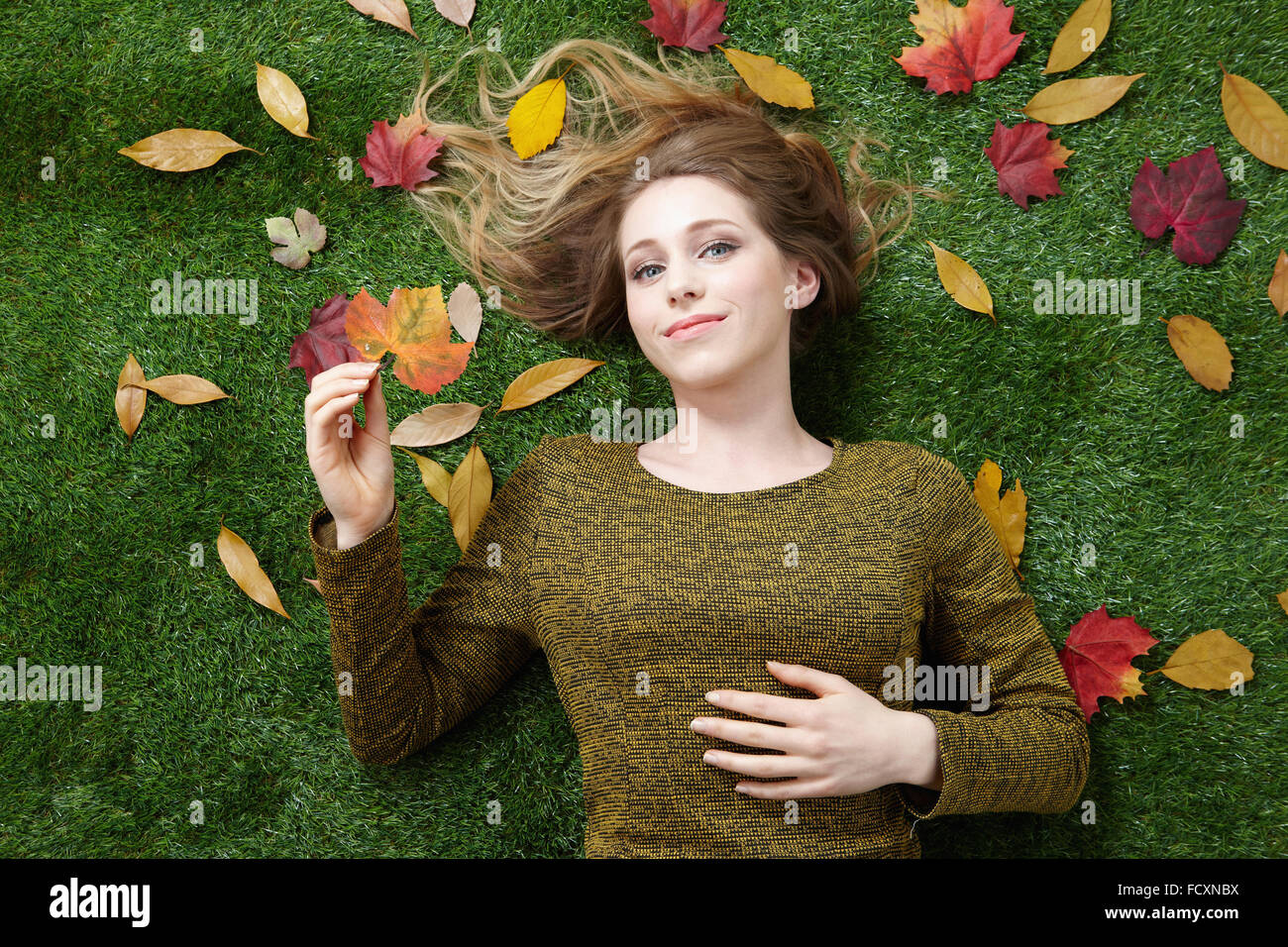 Ritratto di giovane donna sorridente con i capelli lunghi sdraiati sull'erba con foglie cadute, decorrente fino Foto Stock