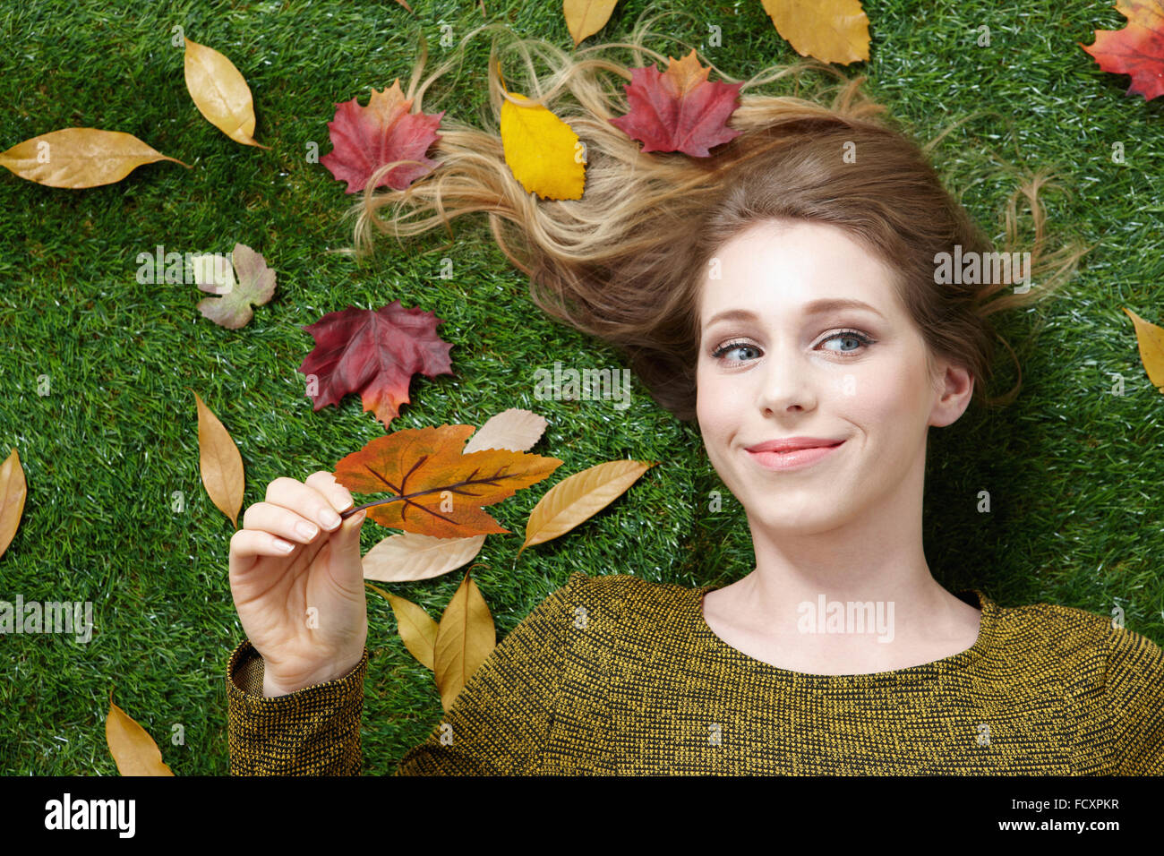 Ritratto di giovane donna sorridente con i capelli lunghi sdraiati sull'erba con foglie cadute, Foto Stock