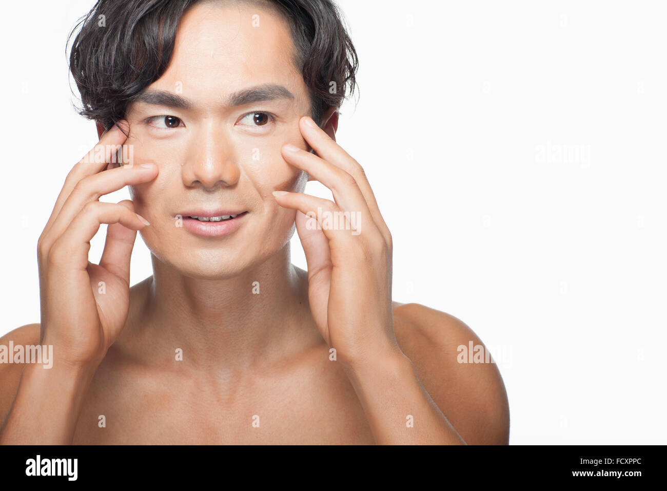 Ritratto di yong uomo sorridente massaggiando il viso con le mani Foto Stock