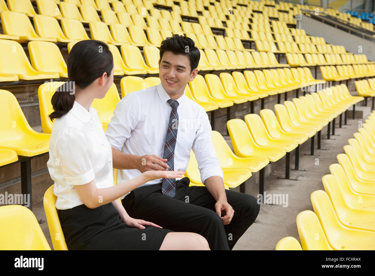 Uomo sorridente e la donna in abiti seduti sui sedili dello stadio e parlare faccia a faccia Foto Stock