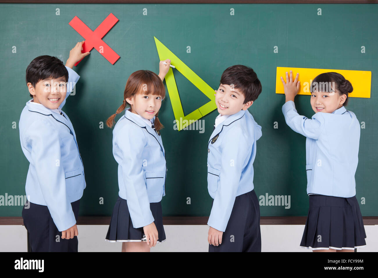 Quattro gli studenti della scuola elementare di trattenimento di un oggetto correlato alla matematica ciascuna e metterle sulla lavagna tutti guardando indietro Foto Stock