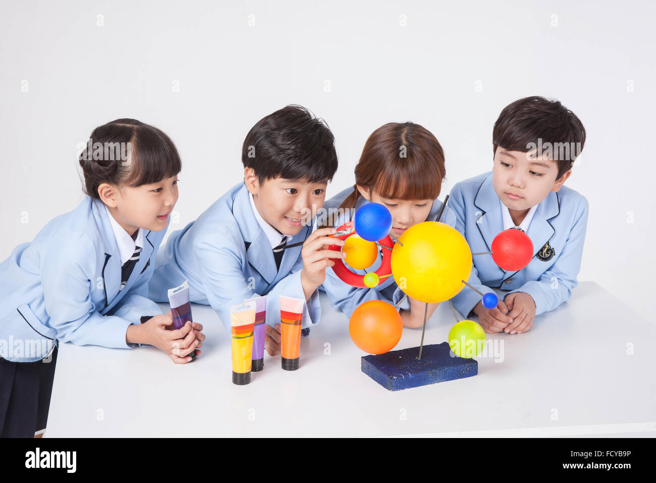 Quattro gli studenti della scuola elementare al banco di colorare il pianeta modello con vernici di colore Foto Stock