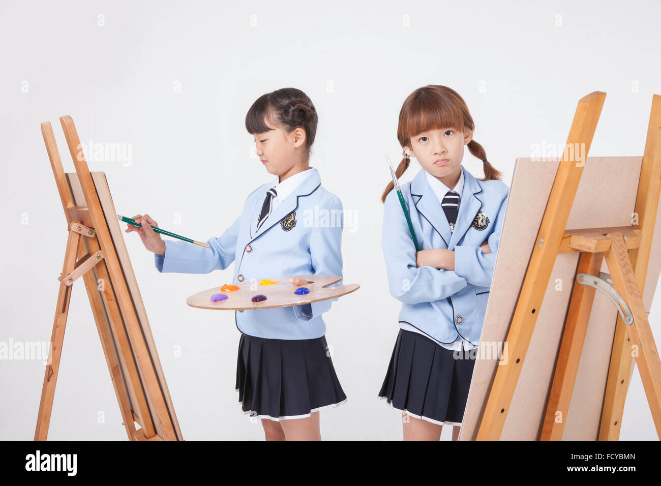 Scuola elementare di disegno ragazza con gli strumenti di disegno e l'altra ragazza con un cavalletto con lo sguardo in avanti con le braccia piegate sia in Foto Stock