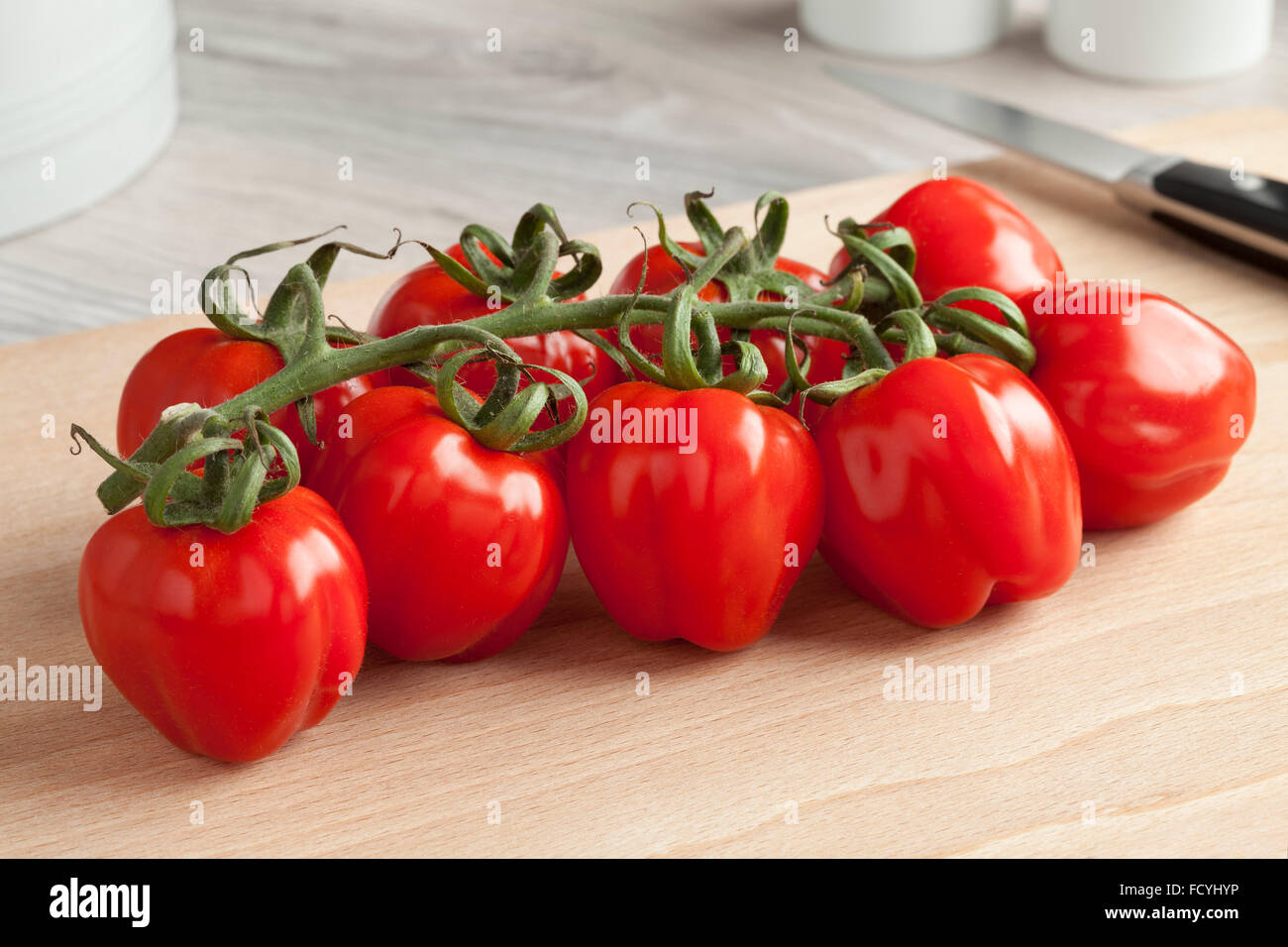 Freschi pomodori rossi su una vite su un tagliere Foto Stock
