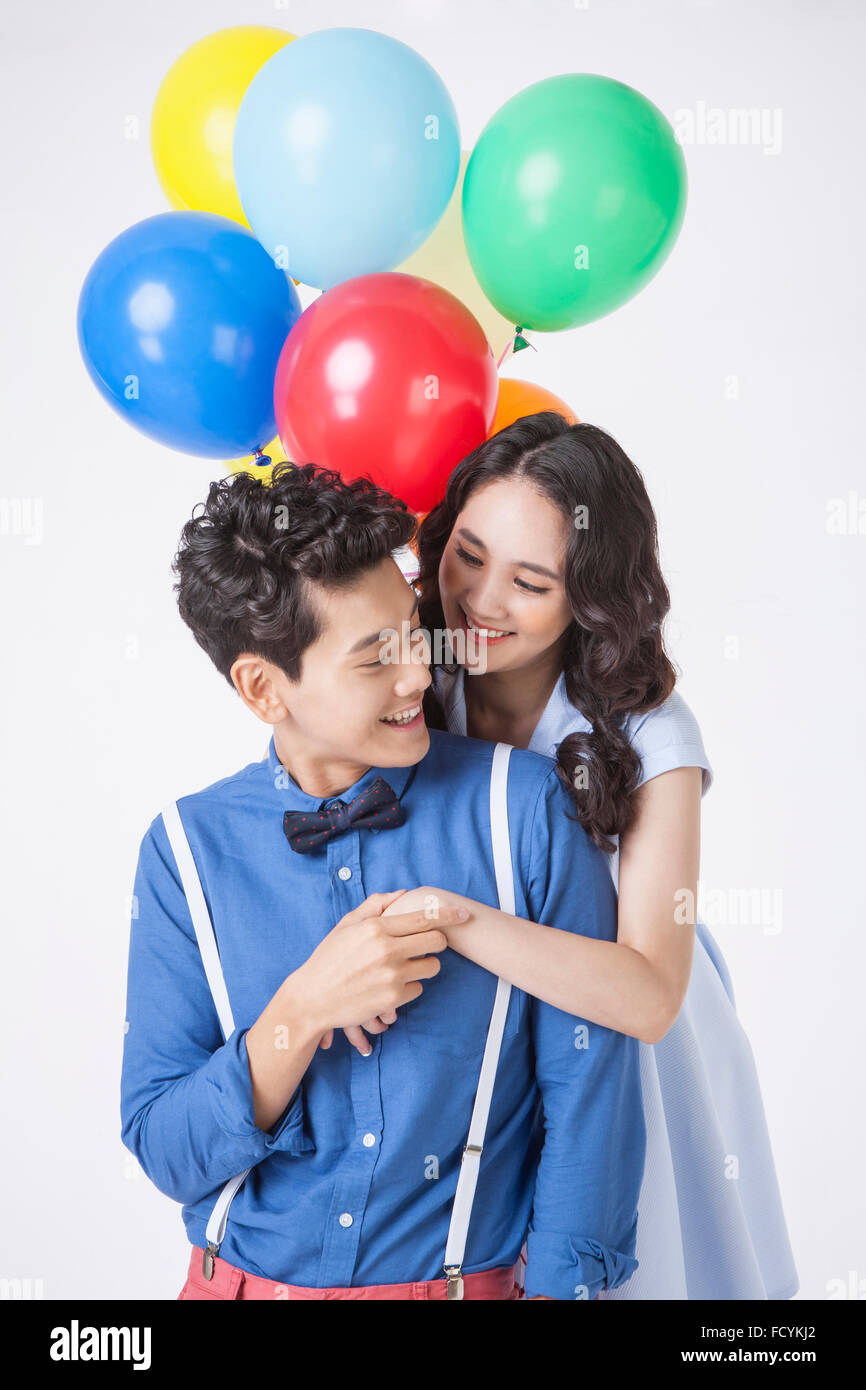 Donna con palloncini colorati costeggiata da dietro un uomo e sia in abiti casual e guardando a vicenda con un sorriso Foto Stock