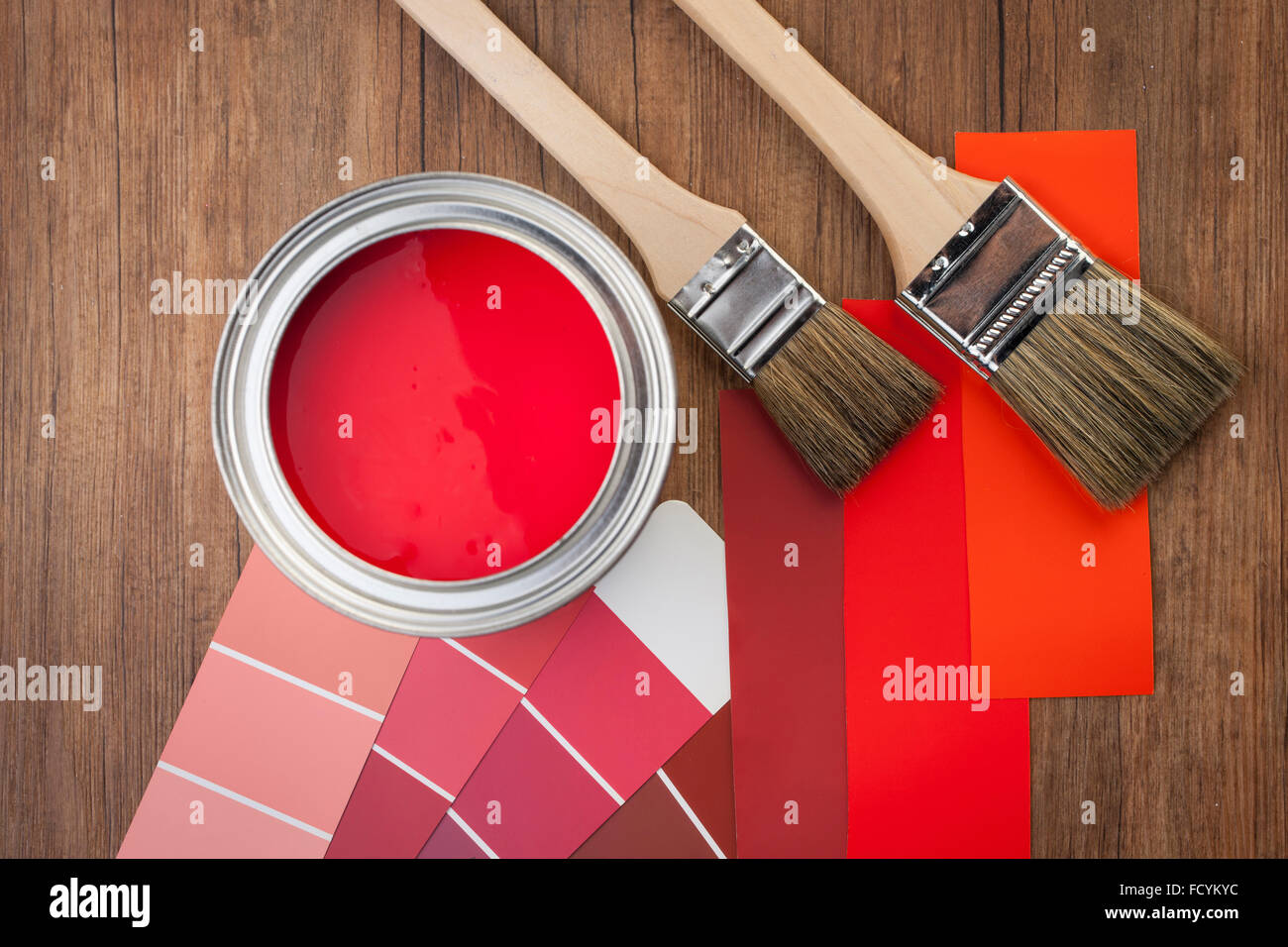 Elevato angolo di vernice rossa pot e lo schema di colori in tonalità di rosso con pennelli per dipingere su uno sfondo di legno Foto Stock