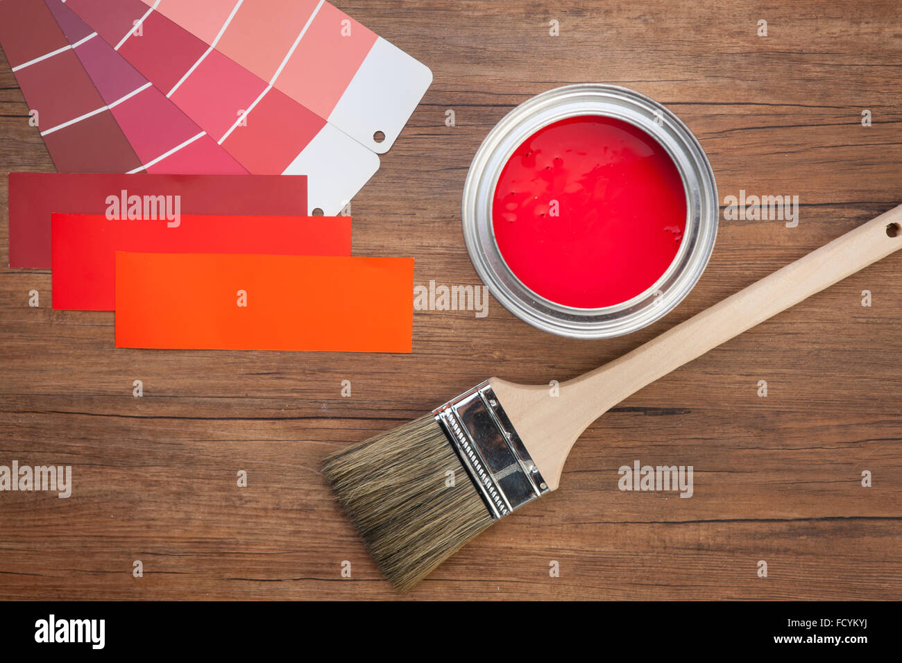 Elevato angolo di schema colori in tonalità di rosso e rosso vaso di vernice con una spazzola di vernice su uno sfondo di legno Foto Stock