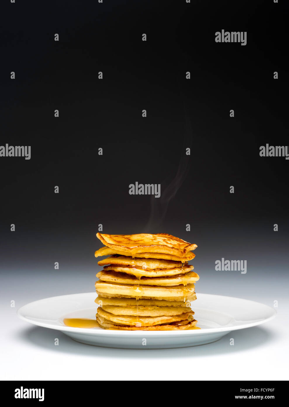 Pila di frittelle sulla piastra bianca spruzzata con sciroppo Foto Stock