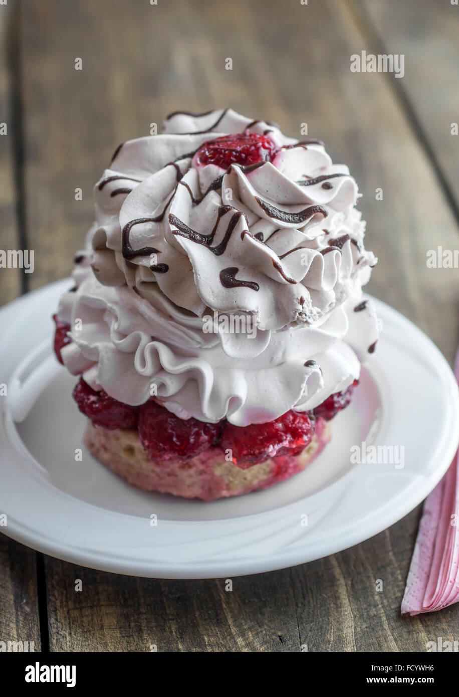 Unico cupcake alla vaniglia con glassa di formaggio cremoso decorato con ribes rosso e il cioccolato sullo sfondo di legno Foto Stock