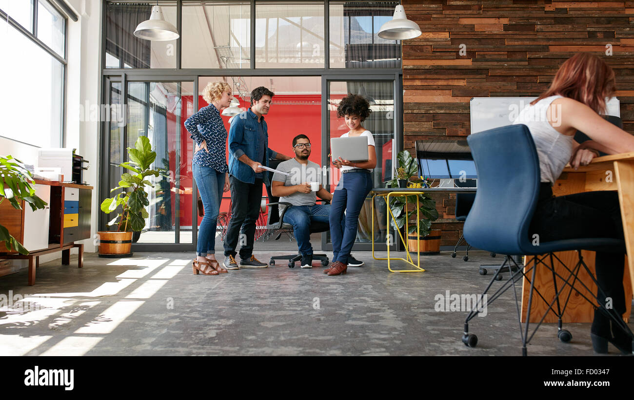 Ritratto di gruppo di persone creative avente un incontro con un computer portatile in un ufficio moderno. La gente di affari aventi conversat rilassata Foto Stock