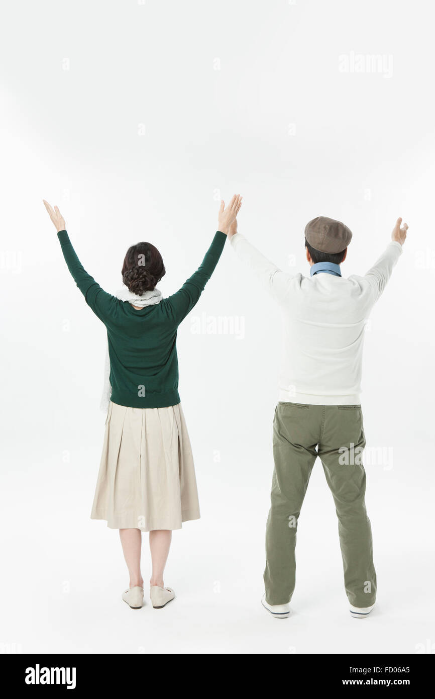 Torna l'aspetto della coppia di mezza età in abiti casual in piedi e alzando le mani in alto Foto Stock
