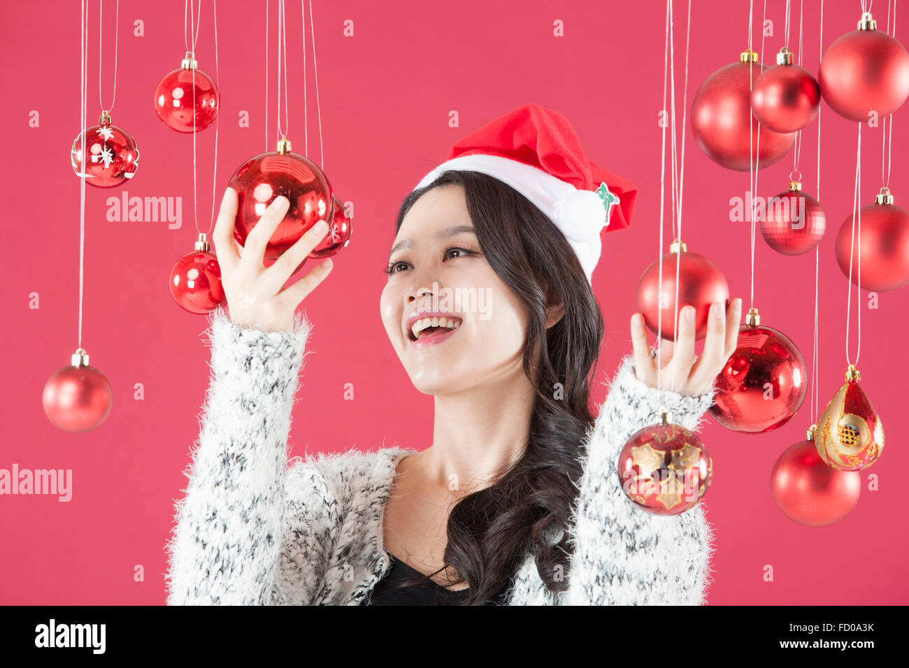 La donna a Santa hat toccando decorazione di Natale che pendevano dal soffitto e lo sta guardando con un sorriso Foto Stock