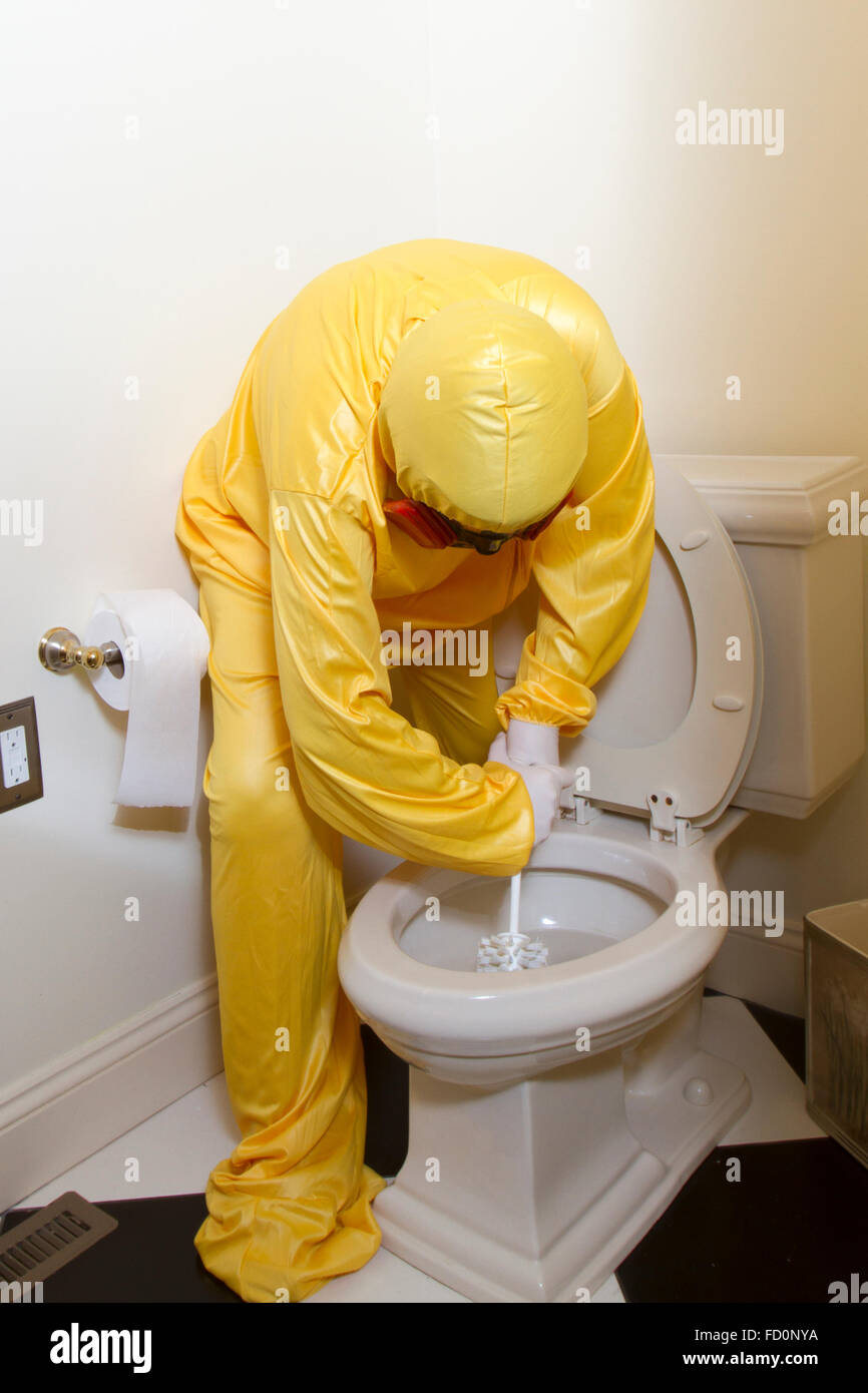 Donna vestita in giallo haz mat uniforme e il ventilatore per la pulizia del bagno wc con spazzola scrub. Foto Stock