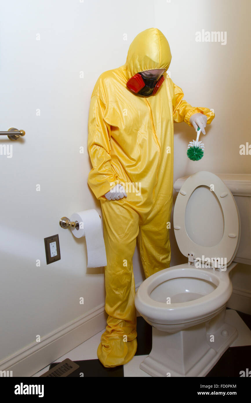 Donna vestita in giallo haz mat uniforme e il ventilatore per la pulizia del bagno wc con spazzola scrub. Foto Stock