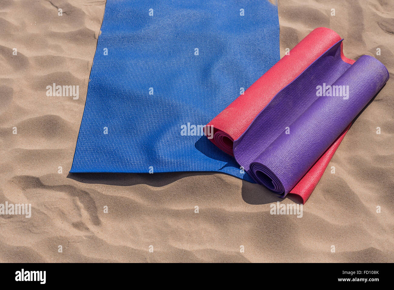 Tre colorati tappeti yoga giacciono sulla sabbia sotto il sole in attesa della lezione: una varietà di attività all'aperto mentre è in vacanza Foto Stock