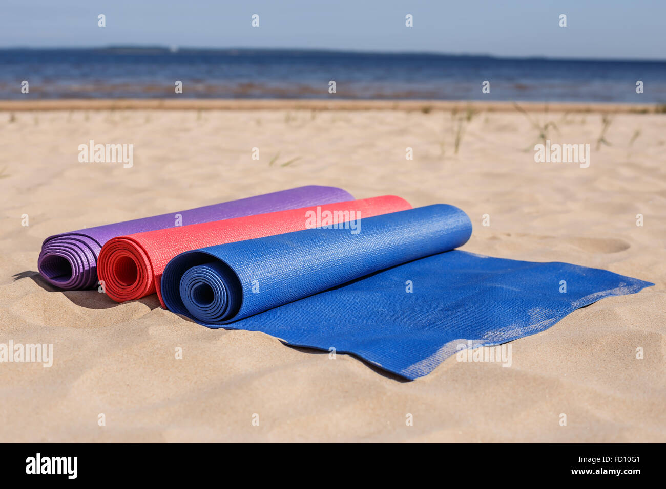 Tre colorati tappeti yoga giacciono sulla sabbia sotto il sole in attesa della lezione: una varietà di attività all'aperto mentre è in vacanza Foto Stock