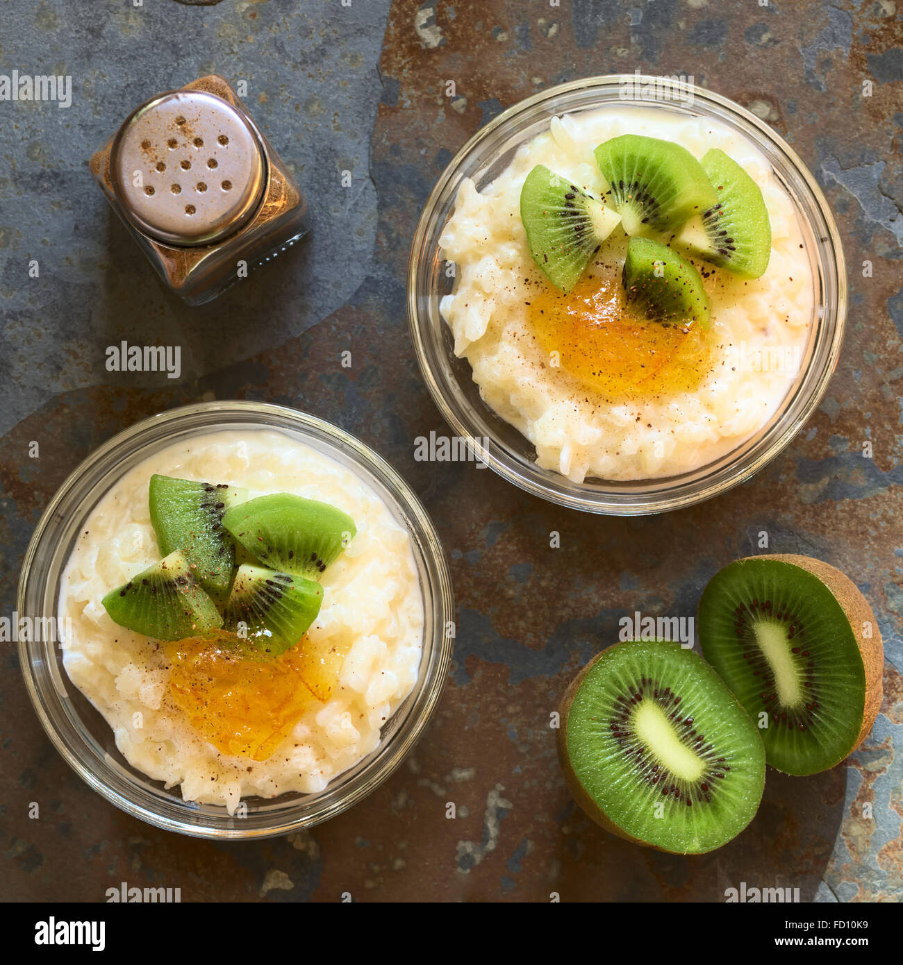 Budino di riso con pezzi di kiwi, marmellata di arancio e cannella in piccole ciotole in vetro, fotografato overhead su ardesia con luce naturale Foto Stock