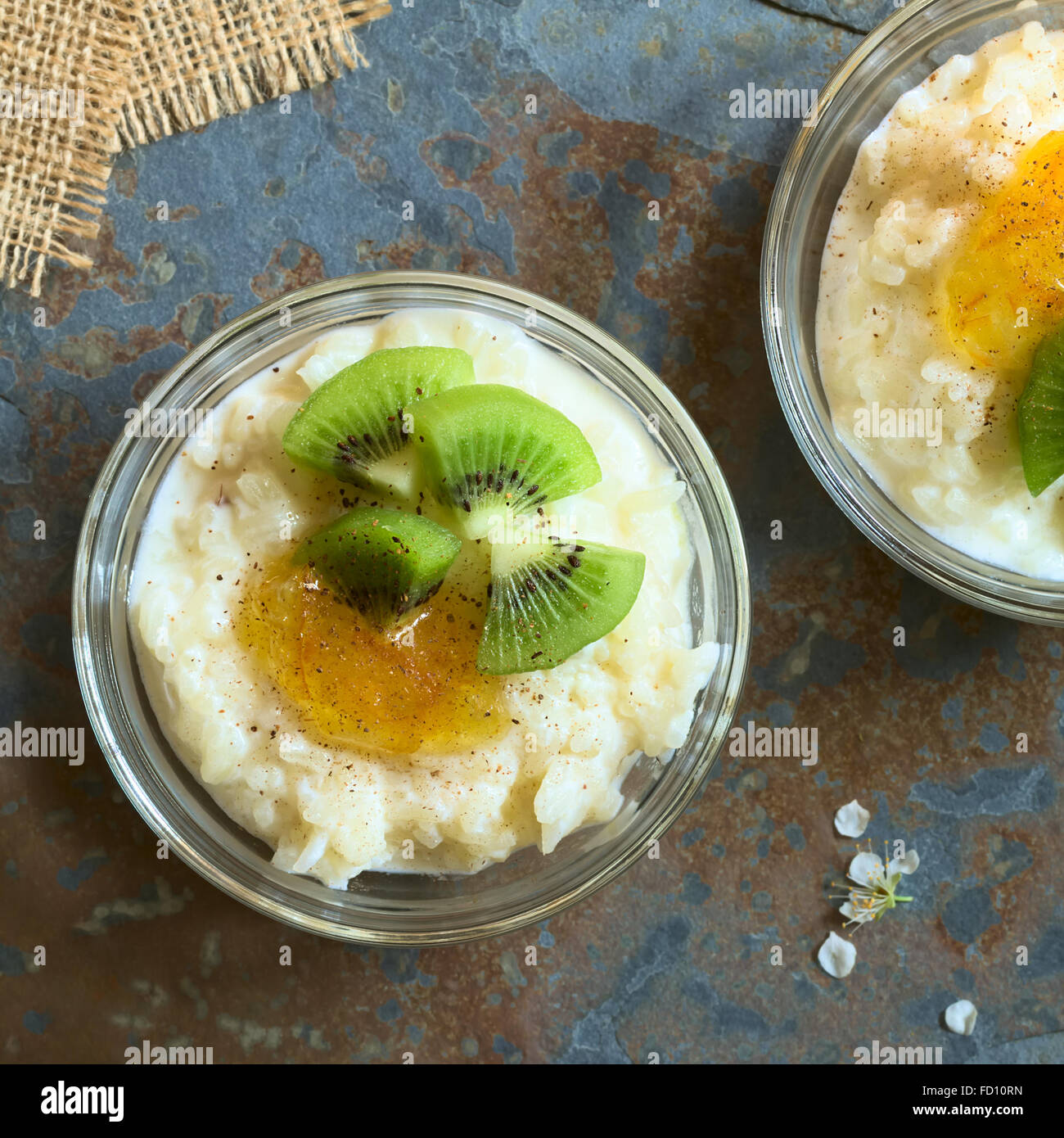 Budino di riso con pezzi di kiwi, marmellata di arancio e cannella in piccola ciotola di vetro, fotografato overhead su ardesia con luce naturale Foto Stock