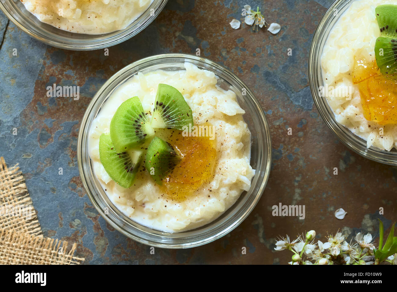 Budino di riso con pezzi di kiwi, marmellata di arancio e cannella in piccola ciotola di vetro, fotografato overhead su ardesia con luce naturale Foto Stock