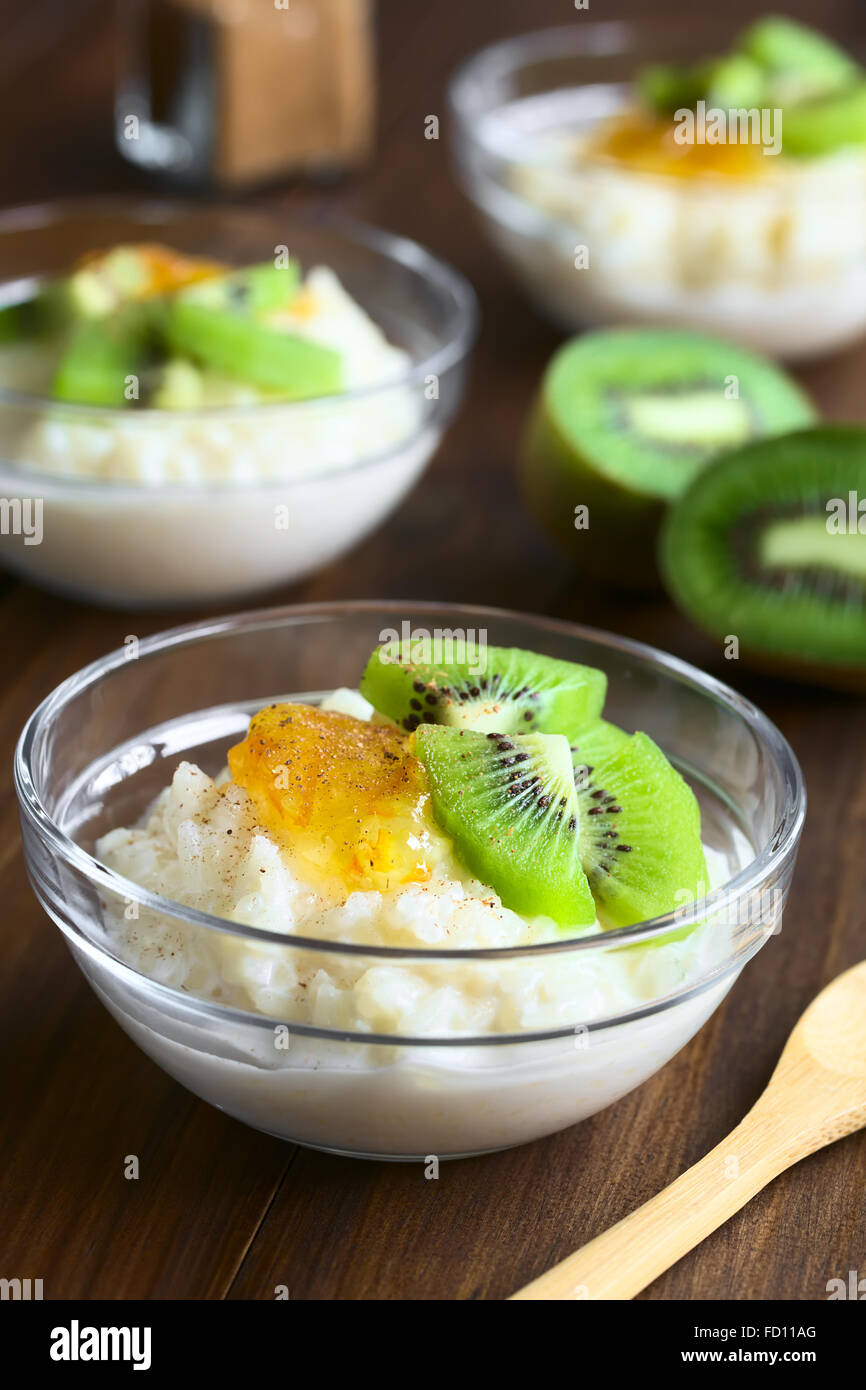 Budino di riso con pezzi di kiwi, marmellata di arancio e cannella in piccole ciotole in vetro, fotografato in legno scuro con luce naturale Foto Stock