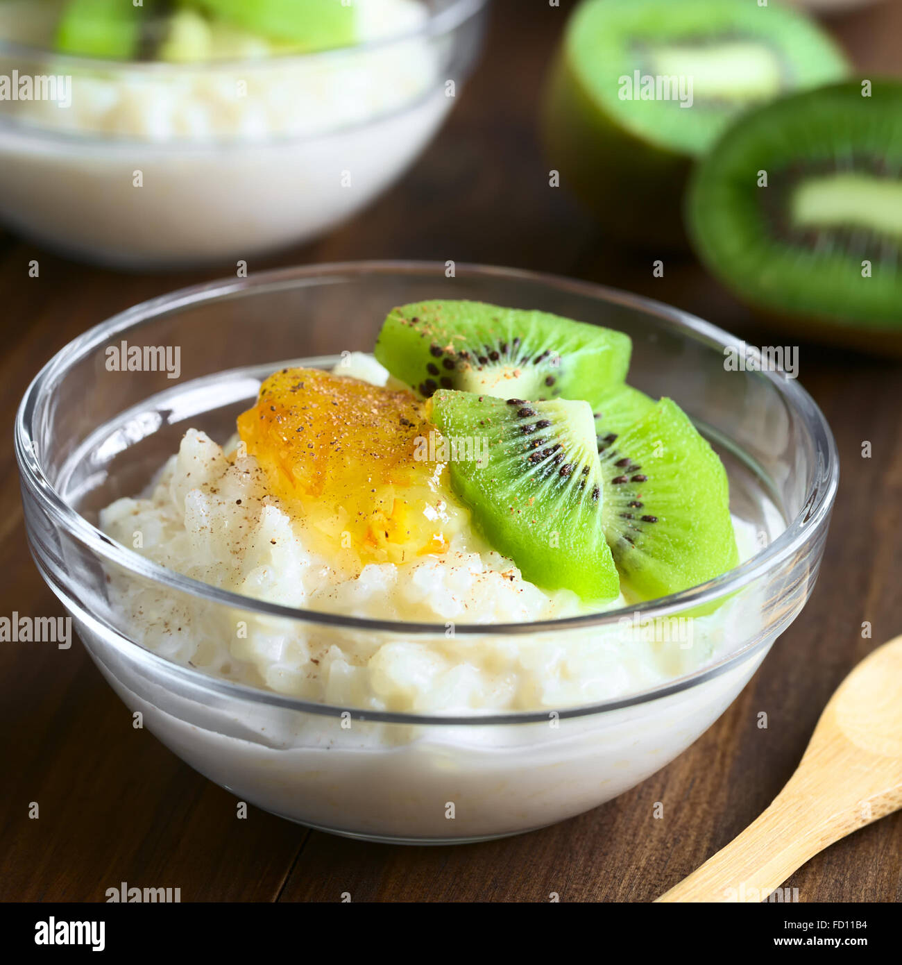 Budino di riso con pezzi di kiwi, marmellata di arancio e cannella in piccola ciotola di vetro, fotografato in legno scuro con luce naturale Foto Stock