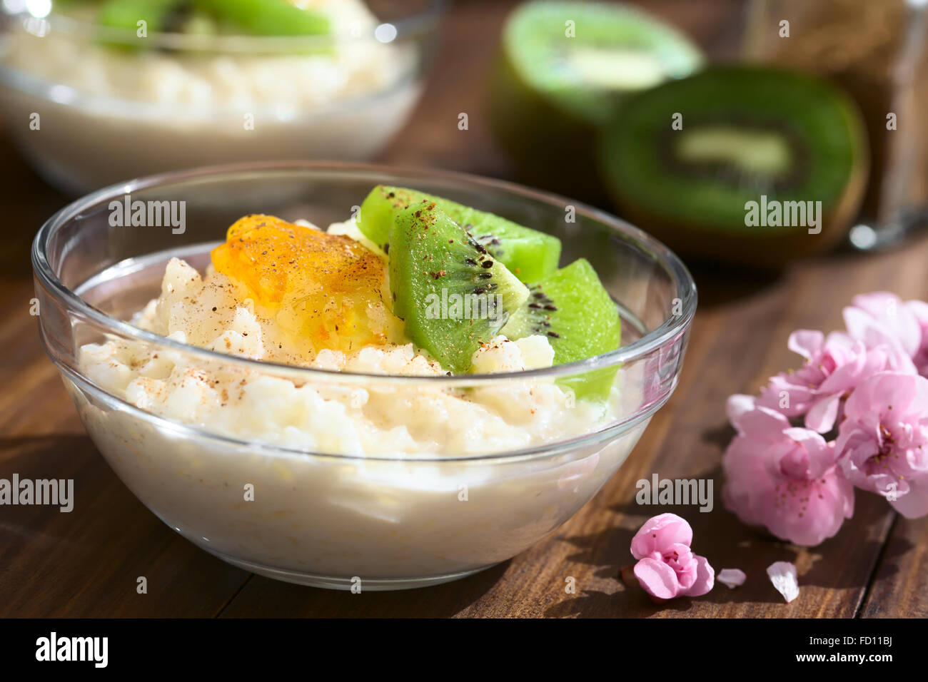 Budino di riso con pezzi di kiwi, marmellata di arancio e cannella in piccola ciotola di vetro, fotografato in legno scuro con luce naturale Foto Stock