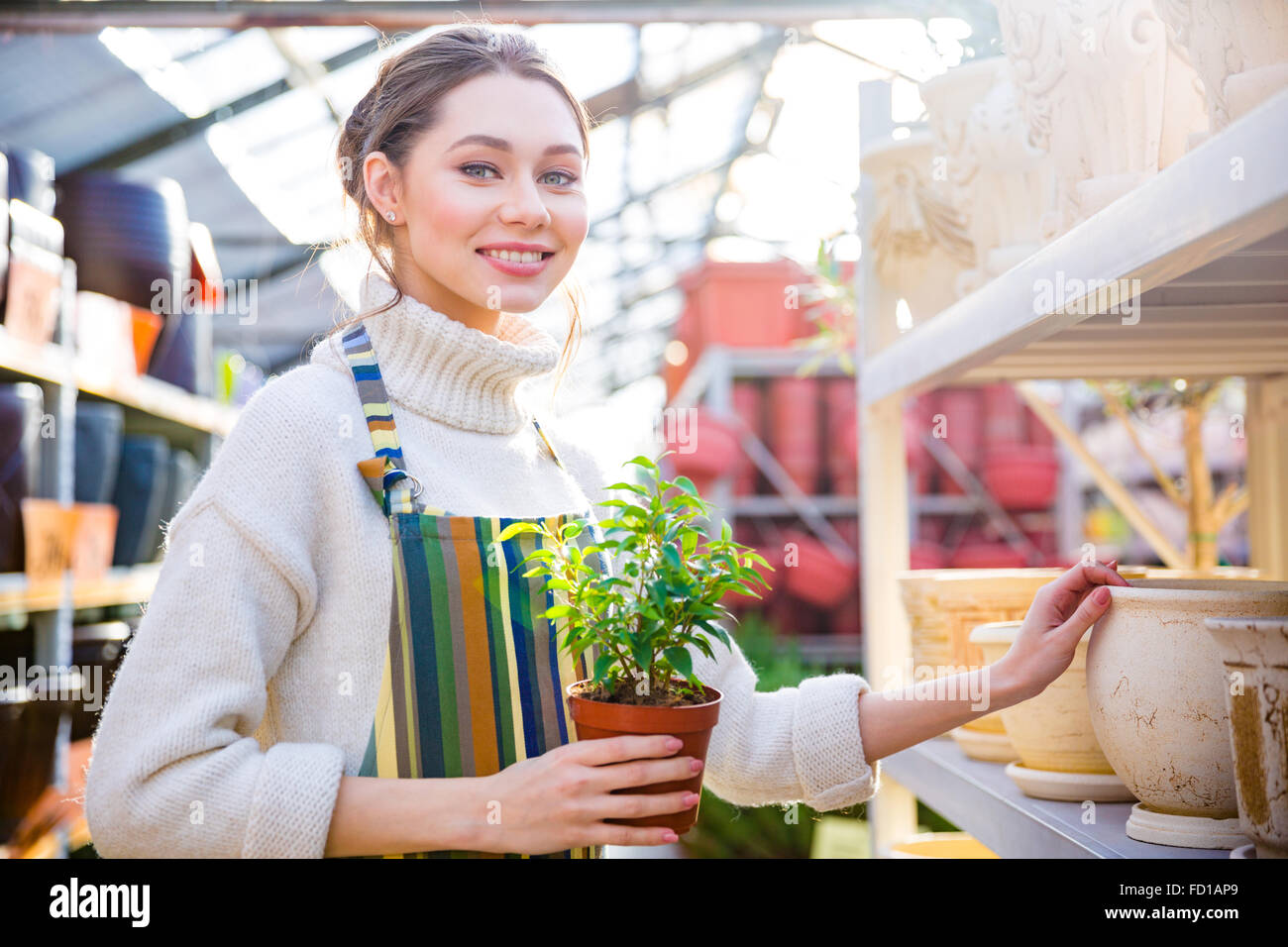 Allegro carino giovane femmina giardiniere in piedi in negozio e scegliendo Nuovo pot per il trapianto la sua pianta piccola Foto Stock