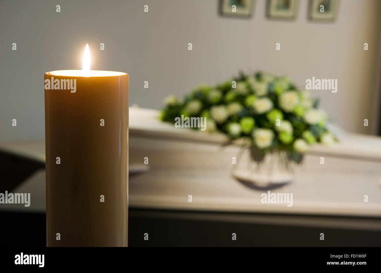 Una candela che brucia con una bara e un omaggio floreale sullo sfondo in una camera mortuaria Foto Stock