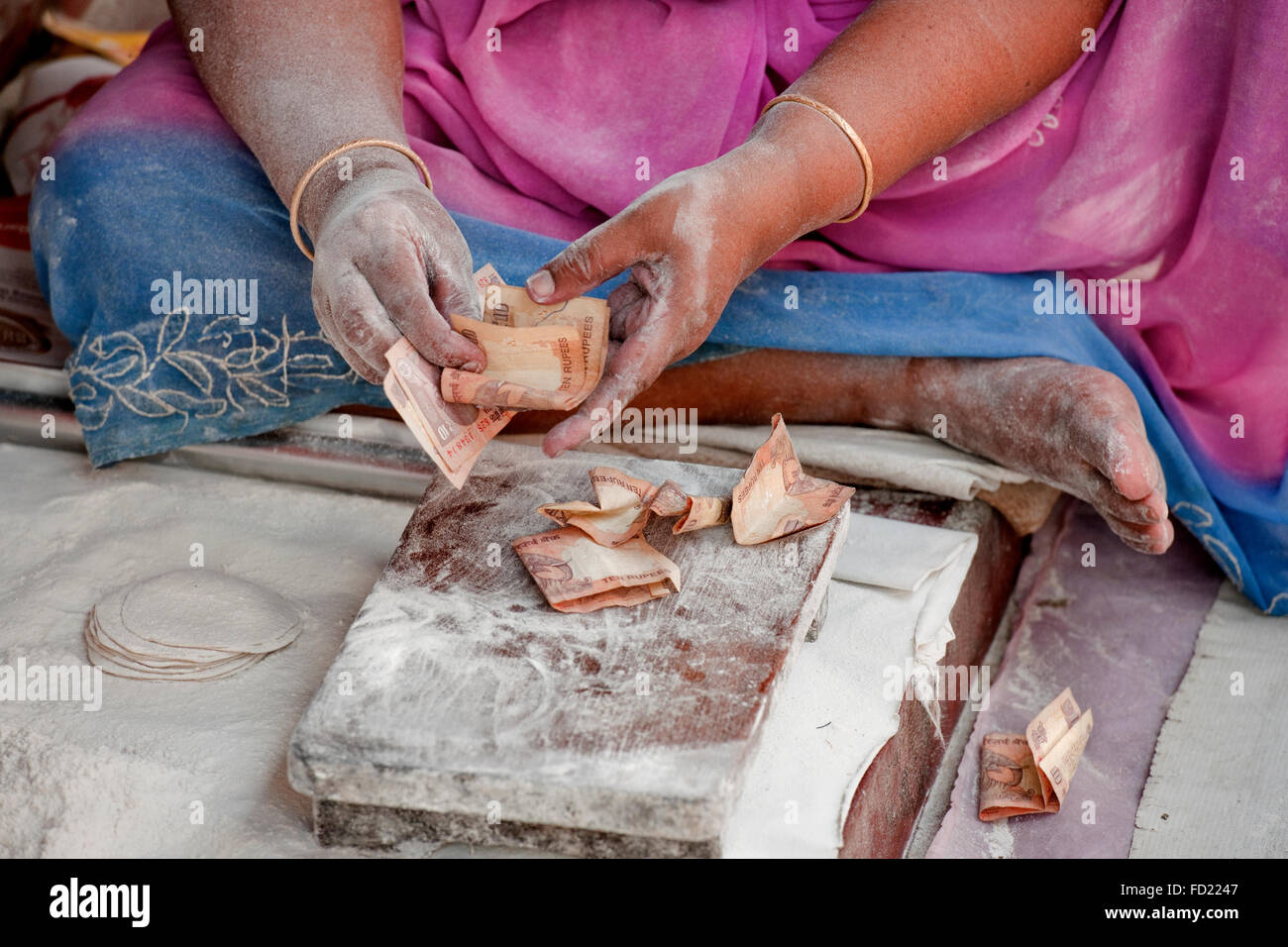 Le mani e le braccia di una donna Indiana contando rupee note su un piano di cottura con materie chappatis e farina Foto Stock