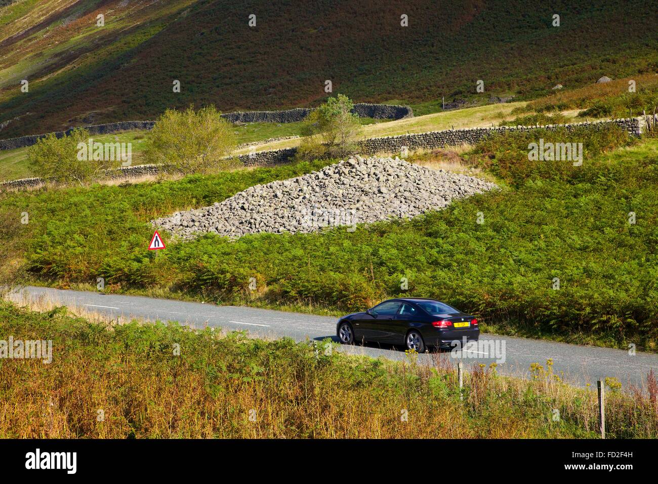 Auto attraversando Dunmail sollevare. Mountain Pass con cairn che è stata sollevata sopra il corpo del Re Dunmail, l'ultimo re di Cumbria. Foto Stock