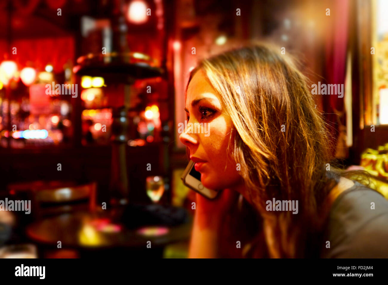 Bella giovane donna seduta da sola guardando preoccupato utilizzando il suo telefono cellulare in un pub o bar REGNO UNITO Foto Stock