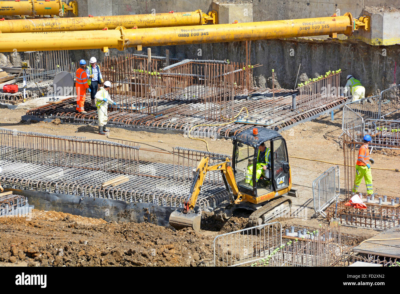 Lavoratori in cantiere costruzione sotto i montanti di rinforzo angolari idraulici gialli sulla parete di ritegno per lavori di fondazione seminterrato Londra Inghilterra Regno Unito Foto Stock