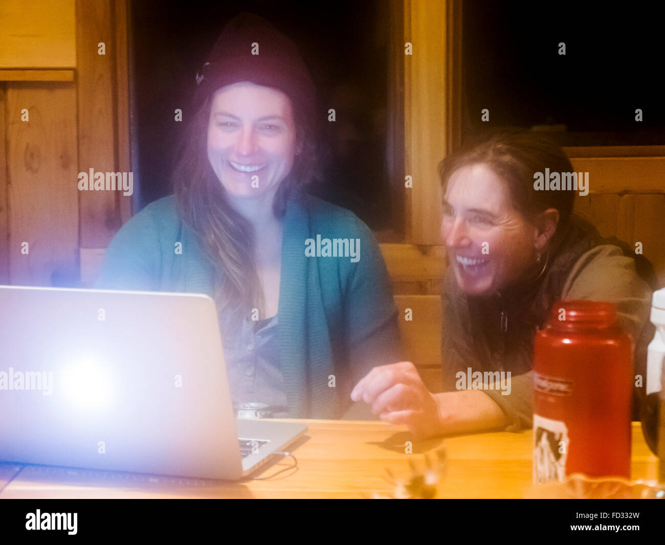 Due femmina paese indietro gli sciatori per visualizzare le fotografie sul computer laptop; all'interno di montaggio remoto Carlyle Lodge; Colombia britannica, Canada Foto Stock