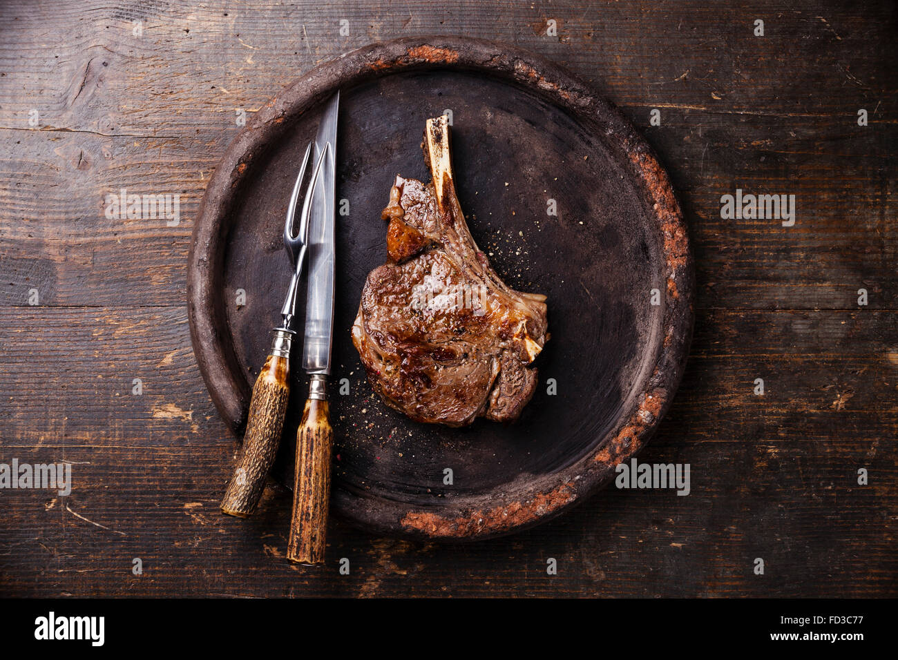 Ribeye sull'osso e coltello e forchetta carving impostato sulla lastra di pietra su sfondo di legno Foto Stock Ribeye sull'osso e coltello e forchetta carving impostato sulla lastra di pietra su sfondo di legno Foto Stock