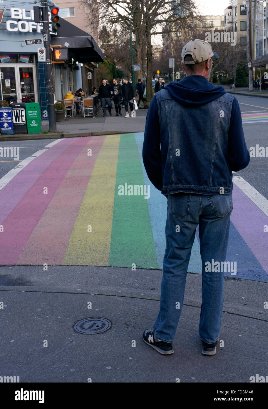 Uomo in attesa di utilizzare il rainbow crosswalk simbolico del Gay Pride nel centro di West End di Vancouver, BC, Canada Foto Stock