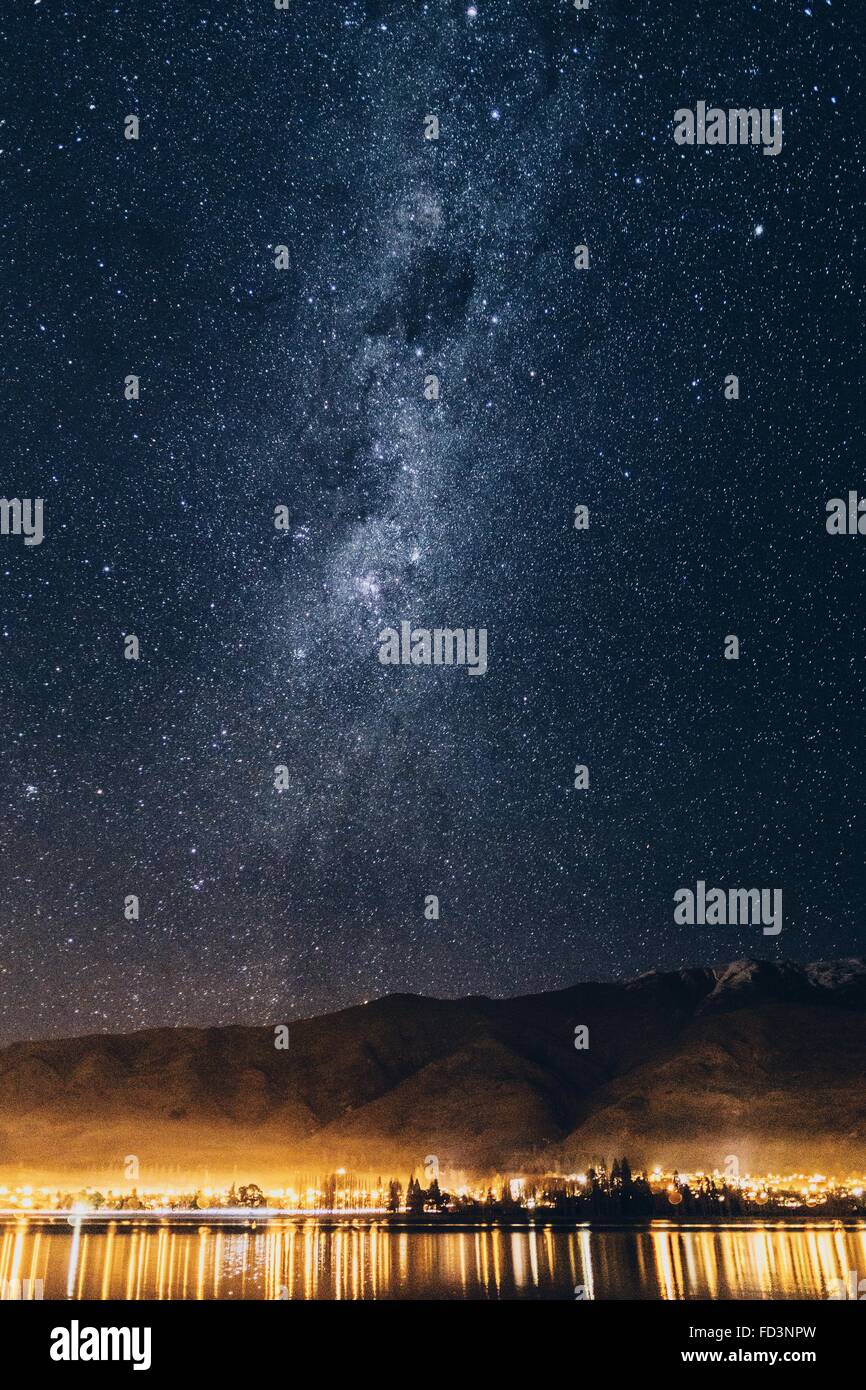 Via lattea oltre il lago Wanaka e montagne durante la notte con le luci della città. Foto Stock