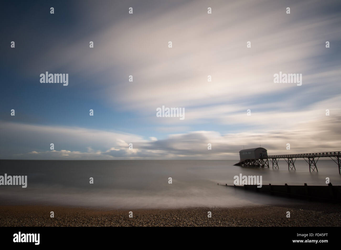 Vista a lunga esposizione su Selsey Lifeboat Station e molo a Sussex, Regno Unito, con mare e nuvole in movimento. Moody astratto. Foto Stock