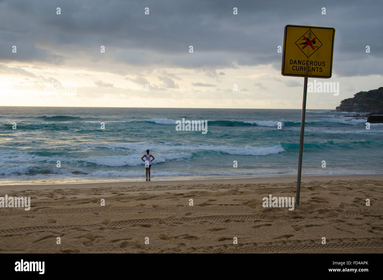 Un pericoloso surf, un cartello di avvertimento e una persona che guarda le onde e l'oceano sulla spiaggia Bondi Sydney, Australia Foto Stock