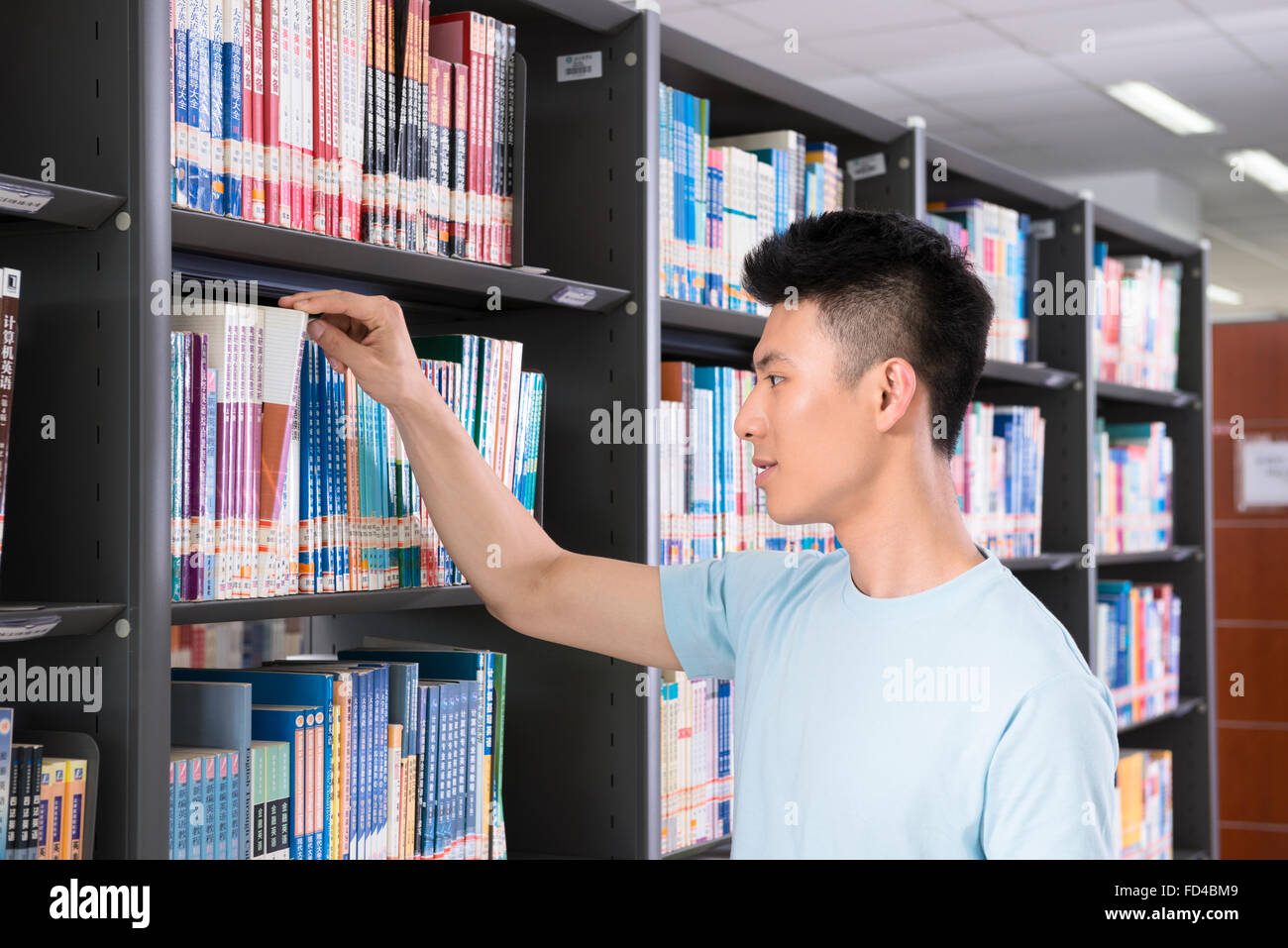 Studente di College selezionando libro dalla biblioteca scaffale Foto Stock