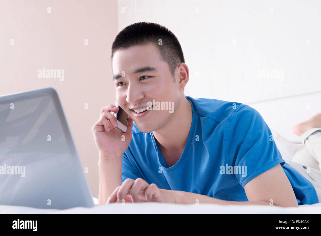 Giovane uomo utilizzando laptop e smart phone nel letto Foto Stock