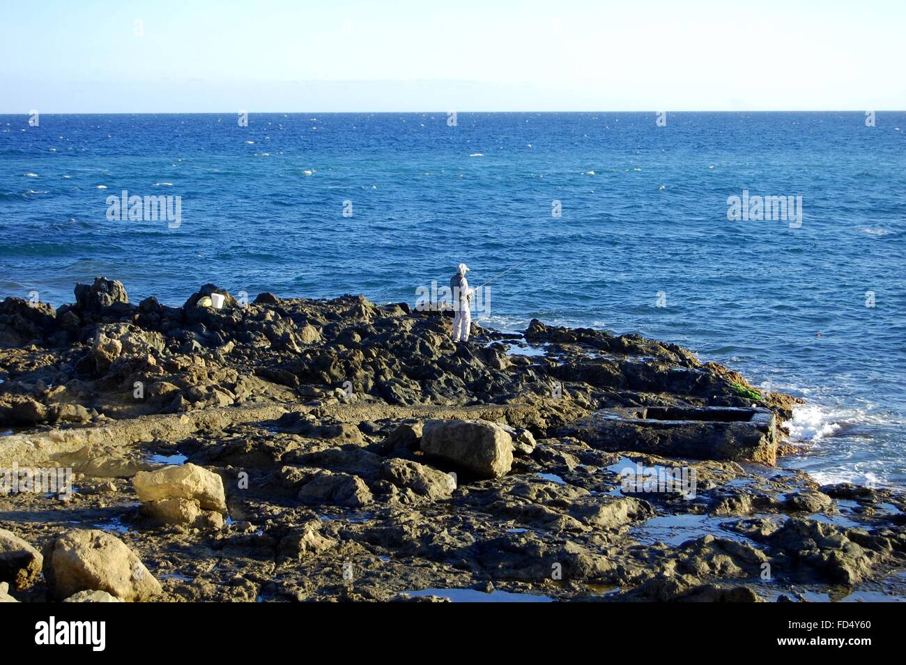 Pescatore sulla crosta oceanica, shore con rocce scure su Gran Canaria isola vulcanica Foto Stock