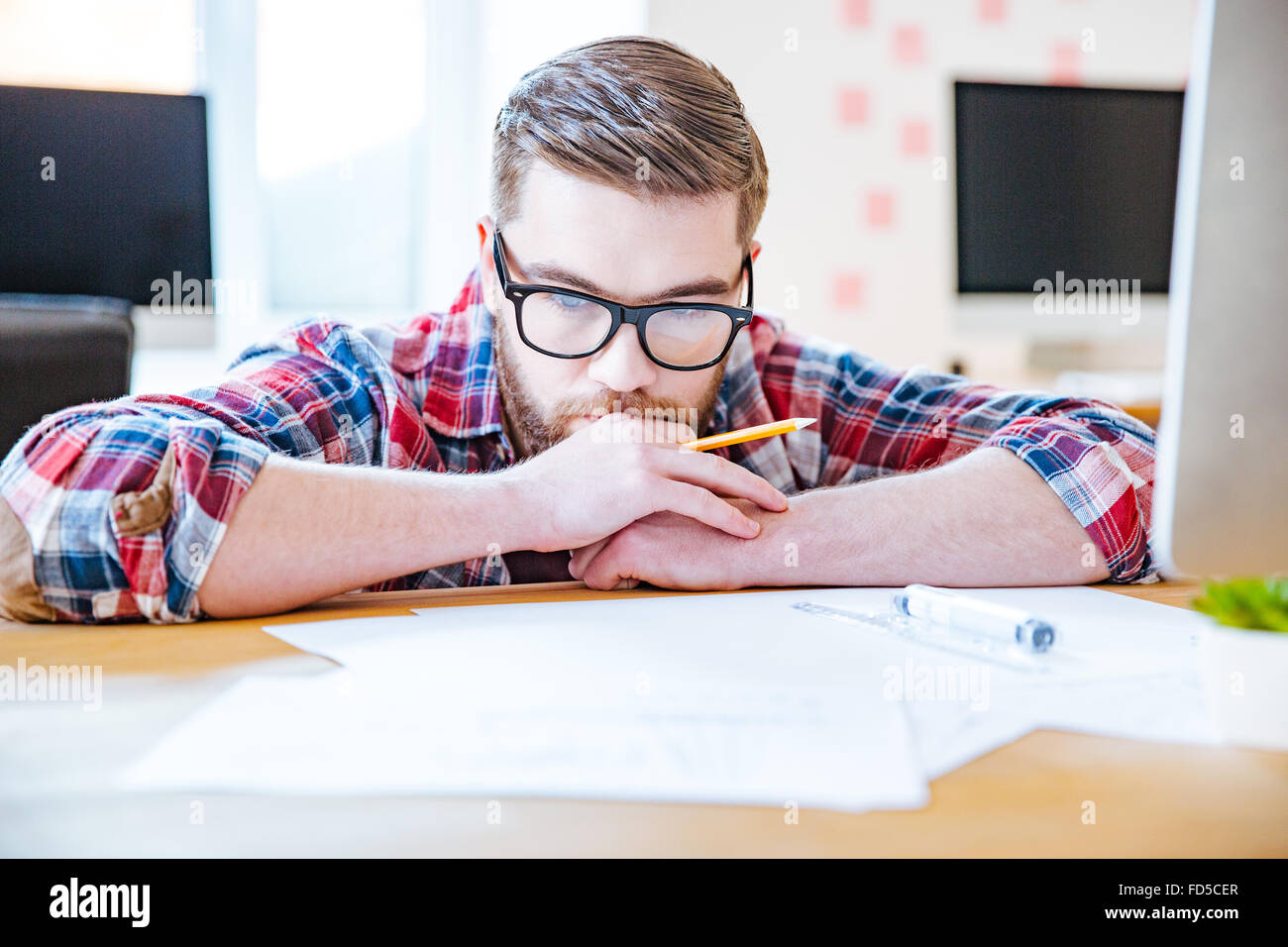 Riflessivo barbuto giovane uomo in bicchieri lavora con blueprits utilizzando una matita e righello in ufficio Foto Stock