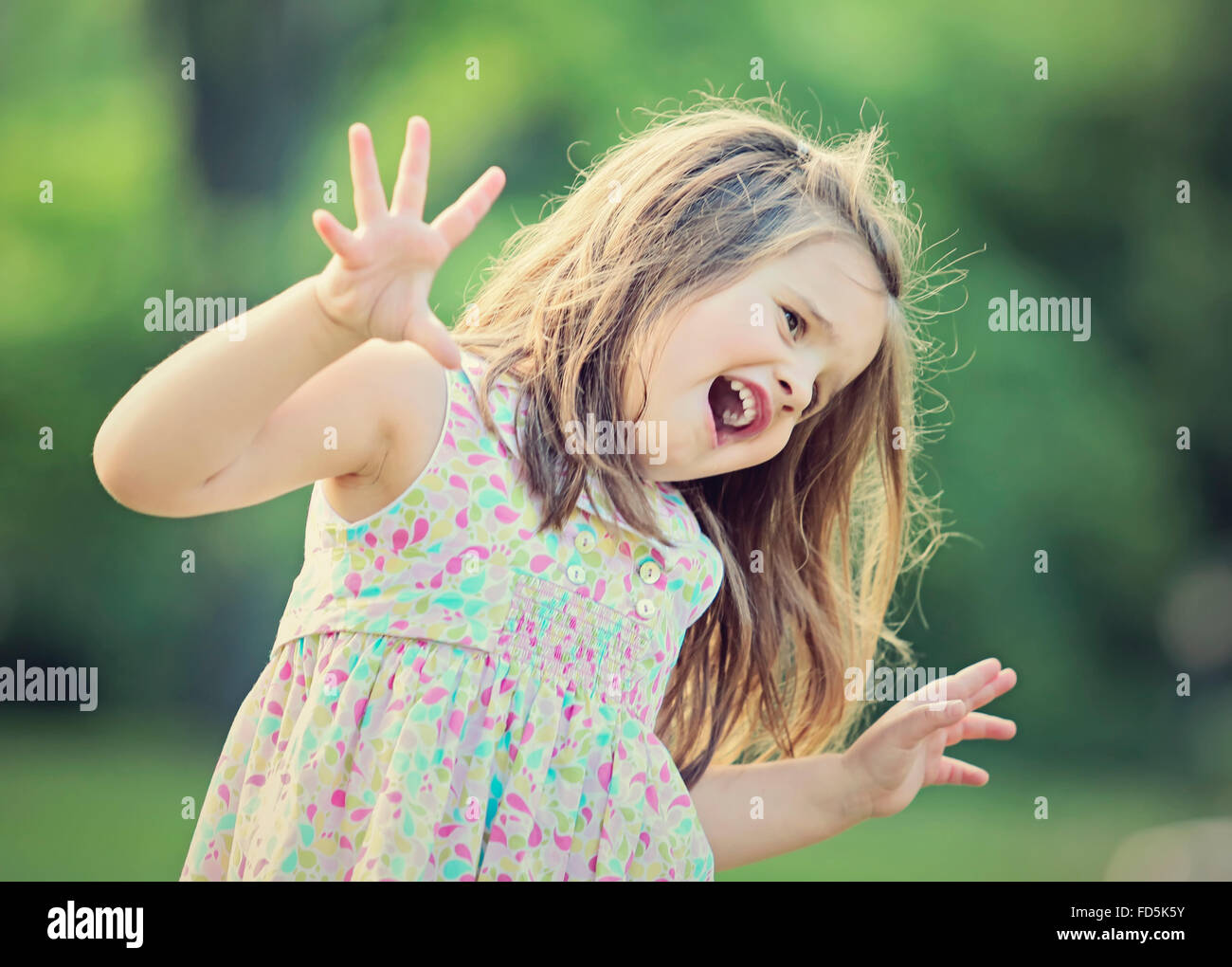 Bambina giocando fuori facendo una buffa faccia ed essendo espressiva con le sue mani. Foto Stock