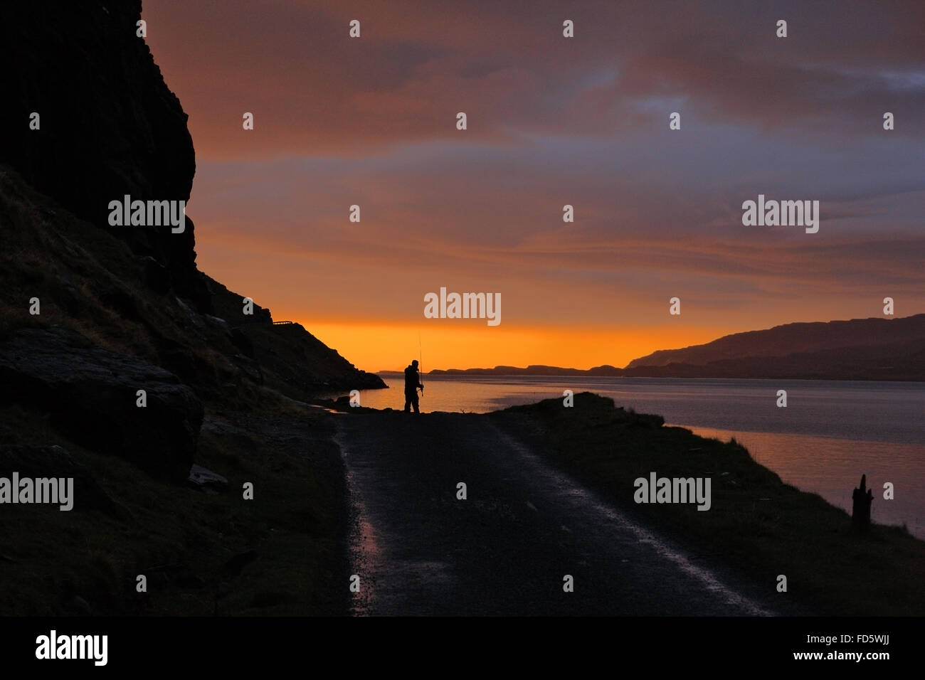 Il pescatore stagliano contro il tramonto in inverno al Gribun rocce sulla Isle of Mull, Scozia Foto Stock