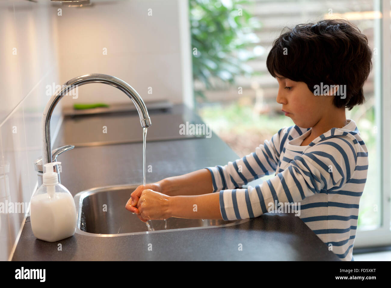 Bambino di otto anni lavaggio delle mani in cucina Foto Stock