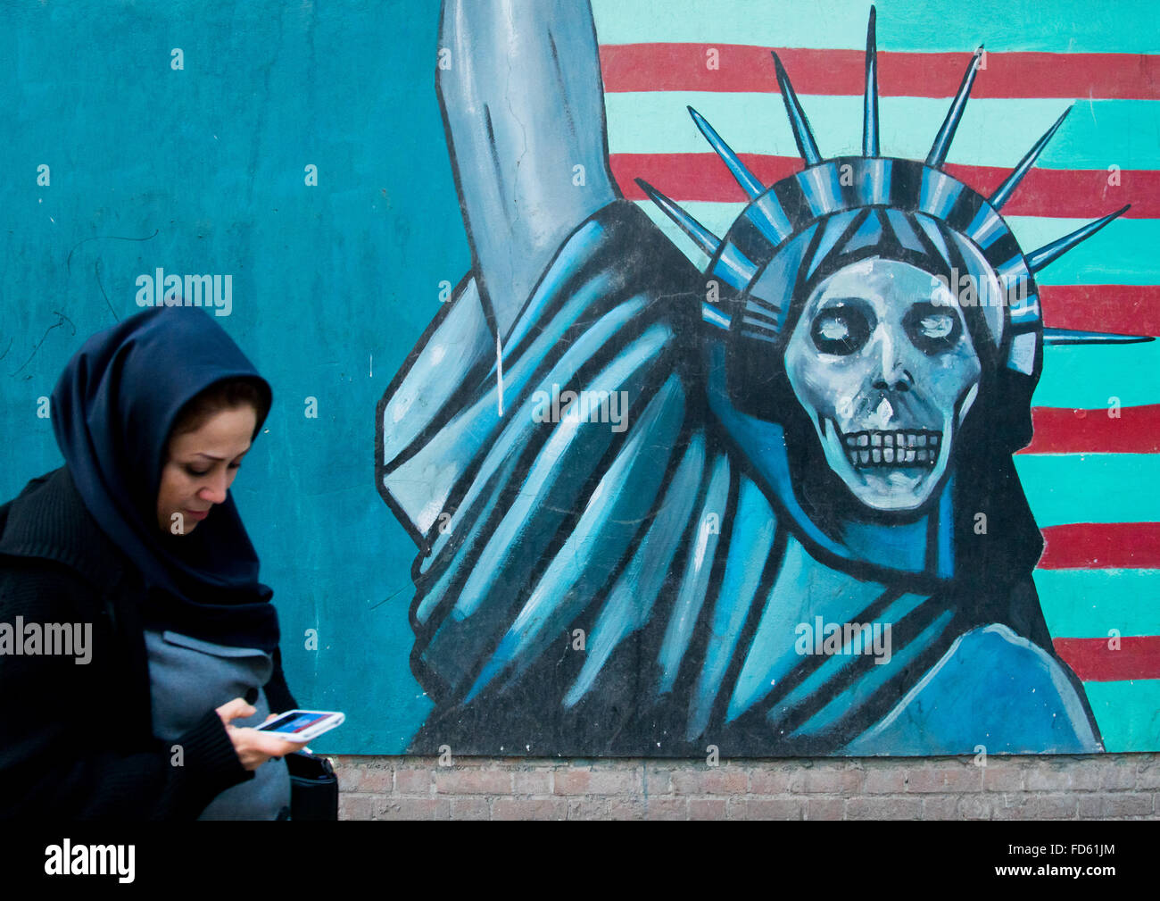 Donna con telefono passando davanti ad un anti-American propaganda slogan statua raffigurante lo scheletro di liberty sulla parete dell'Ambasciata degli Stati Uniti, il distretto centrale, Teheran, Iran Foto Stock