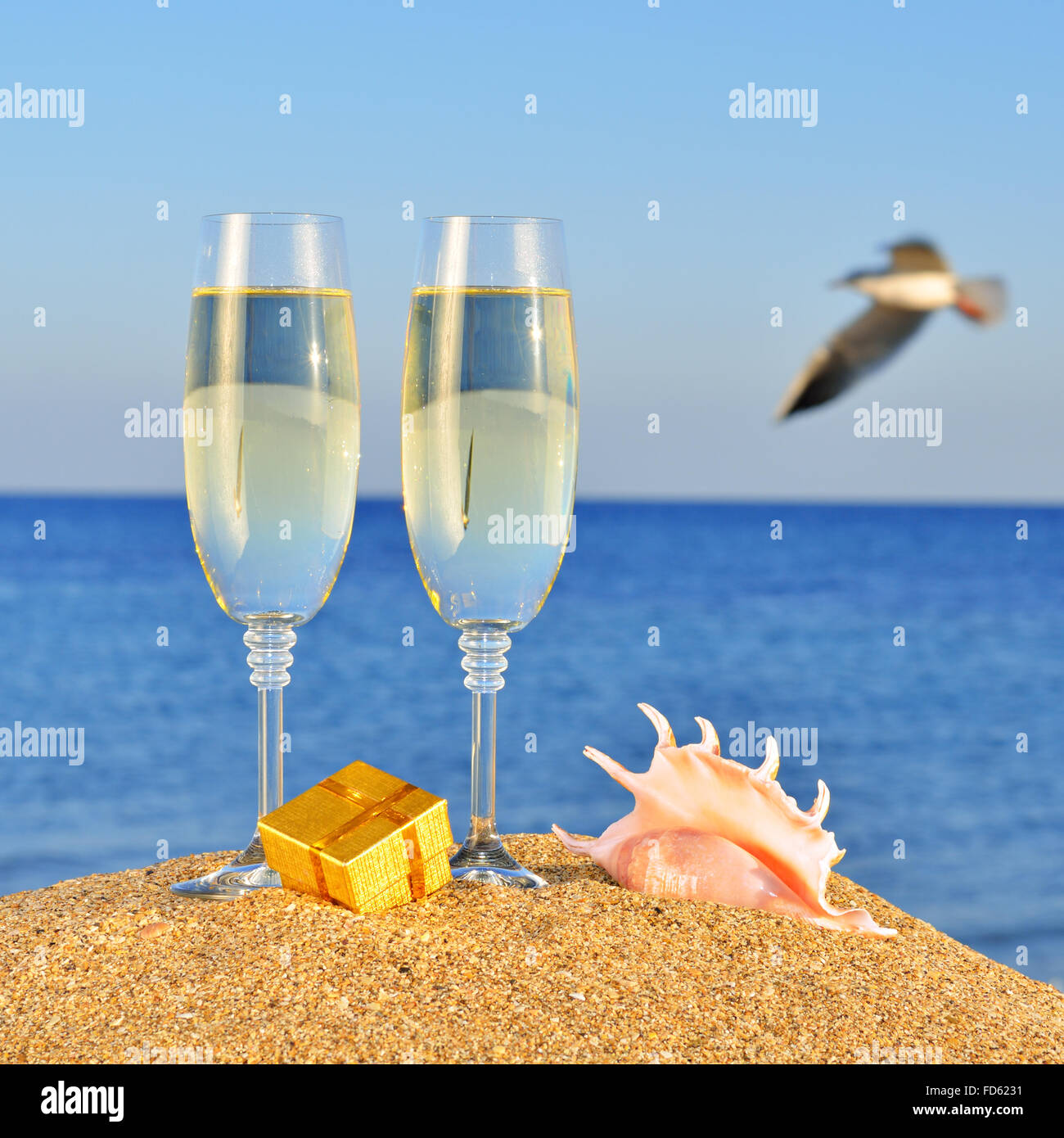 Bicchieri di champagne, box con un regalo e conchiglia sulla spiaggia  contro il cielo e mare blu Foto stock - Alamy