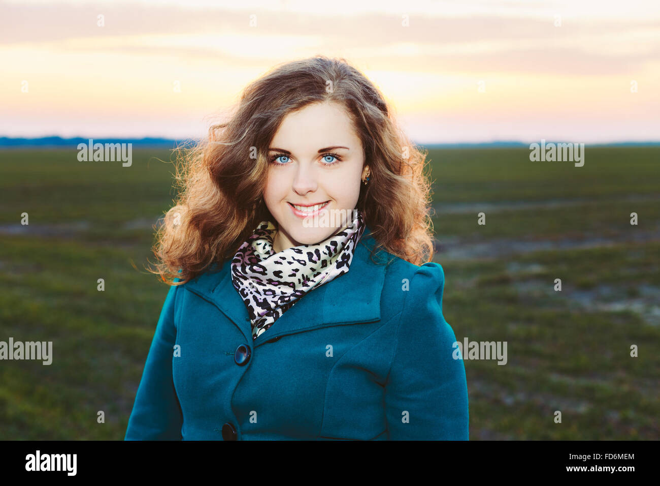 Ritratto di belle dimensioni più giovane donna in Blue Coat in posa di Prato di campo al tramonto sullo sfondo. Molla, ritratto all'aperto Foto Stock